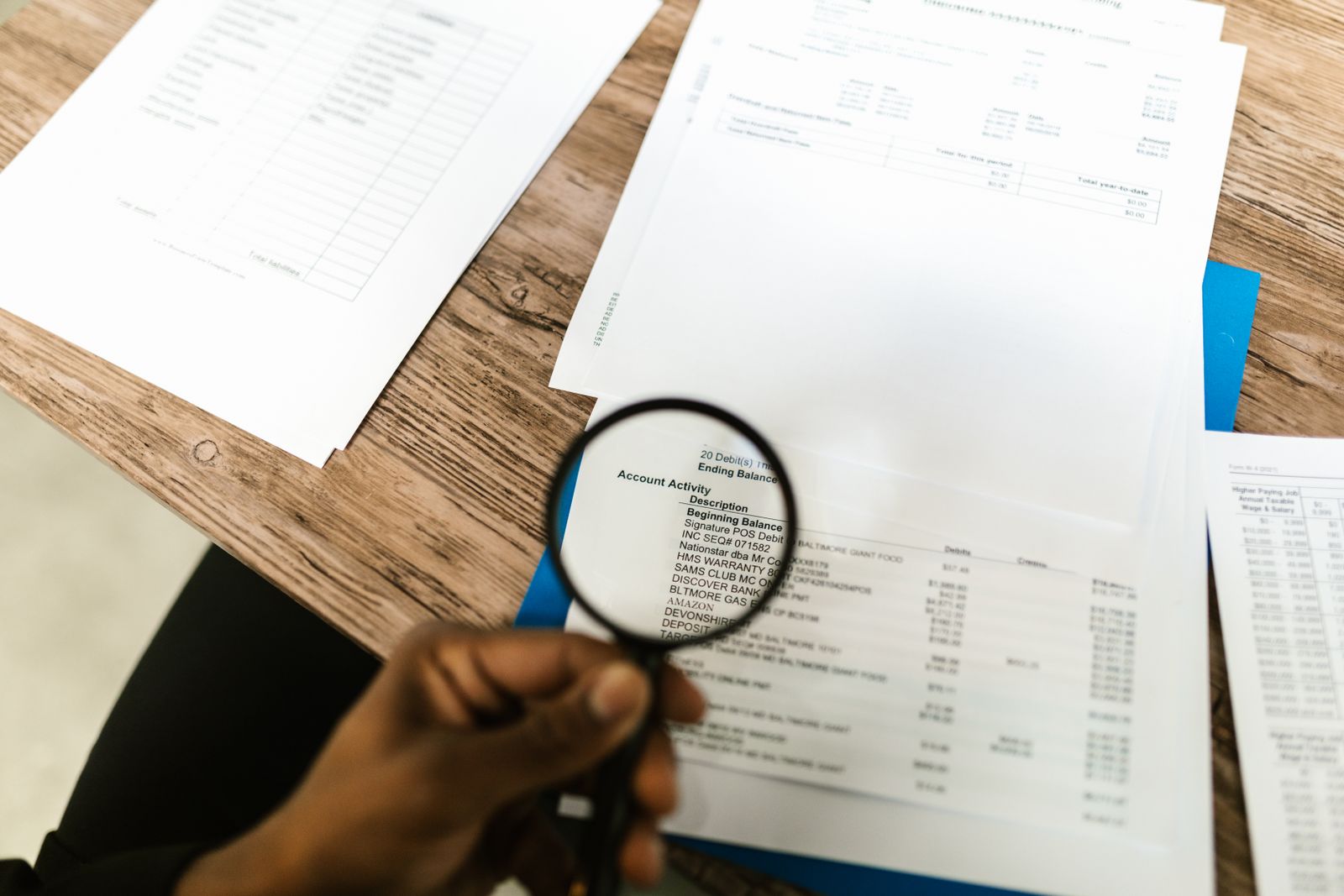 Une main tient une loupe au-dessus de relevés de compte imprimés.